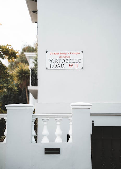 Close-up of a white exterior wall of a building featuring a red and black street sign that reads 'Portobello Road, W.11' registered with the Royal Borough of Kensington and Chelsea. The sign is mounte